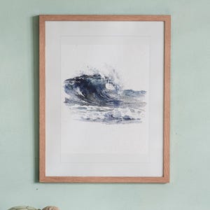 May include: A framed watercolor painting of a crashing ocean wave in shades of deep blue and grey. The artwork is set within a light-toned wooden frame with a white mat border, displaying a dynamic sea scene with white foam and spray.