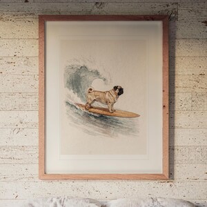 Puede incluir: Una lámina de arte enmarcada que muestra a un pug de color beige con cara negra de pie sobre una tabla de surf de madera. El perro está posicionado frente a una gran ola azul y blanca, representada en estilo acuarela dentro de un marco de madera clara.