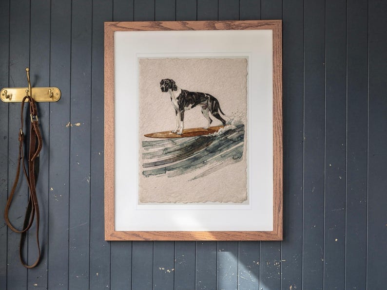 Great Dane Surfing printable art, shown printed in a Red Oak frame with a white mat, hanging above the cubbies in a mudroom.