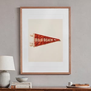 Bells Beach Surf Pennant print in a Red Oak frame with a white mat, hanging above the sideboard in a mid-century living room.