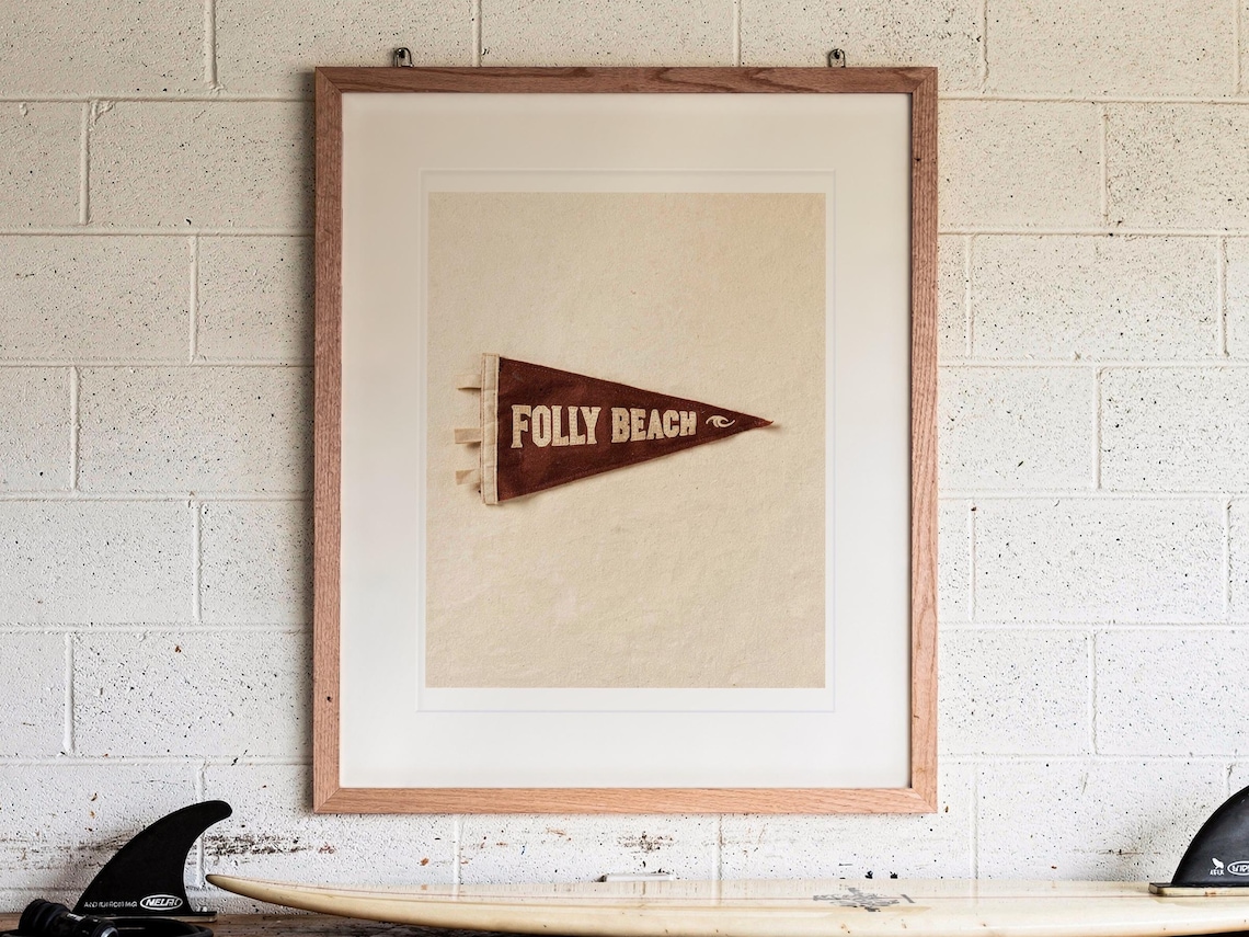 Folly Beach Surf Pennant print in a Red Oak frame with a white mat, hanging above the workbench in a surf garage.
