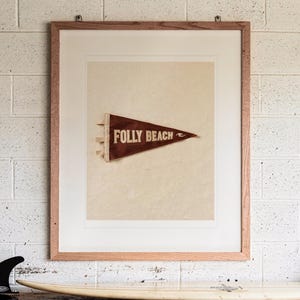 Folly Beach Surf Pennant print in a Red Oak frame with a white mat, hanging above the workbench in a surf garage.