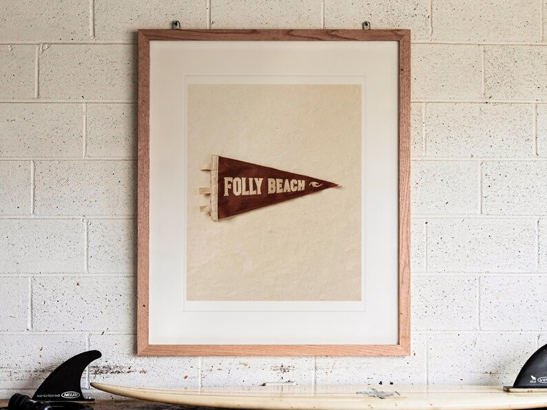 Folly Beach Surf Pennant print in a Red Oak frame with a white mat, hanging above the workbench in a surf garage.