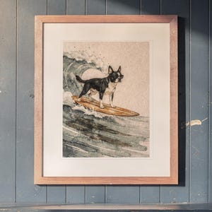 Boston Terrier Surfing printable art, shown printed in a Red Oak frame with a white mat, hanging above the cubbies in a mudroom.