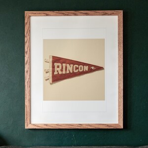 Rincon Surf Pennant print in a Red Oak frame with a white mat, hanging above the cabinet in a game room.