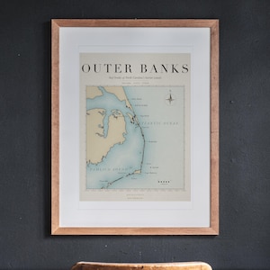 Outer Banks Surf Map printable art, shown printed in a Red Oak frame with a white mat, hanging above the desk in a home office.