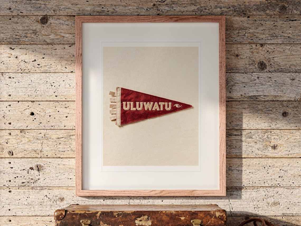 Uluwatu Surf Pennant print in a Red Oak frame with a white mat, hanging above the trunk in a beach house loft.