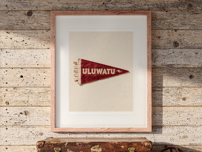 Uluwatu Surf Pennant print in a Red Oak frame with a white mat, hanging above the trunk in a beach house loft.