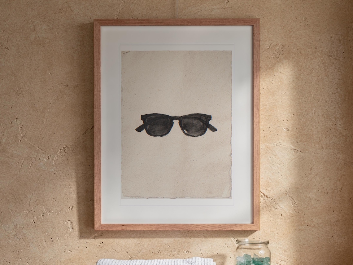 Wayfarer Sunglasses Sumi-e Ink print in a Red Oak frame with a white mat, hanging above the vanity in a bright bathroom.