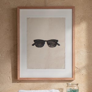 Wayfarer Sunglasses Sumi-e Ink print in a Red Oak frame with a white mat, hanging above the vanity in a bright bathroom.