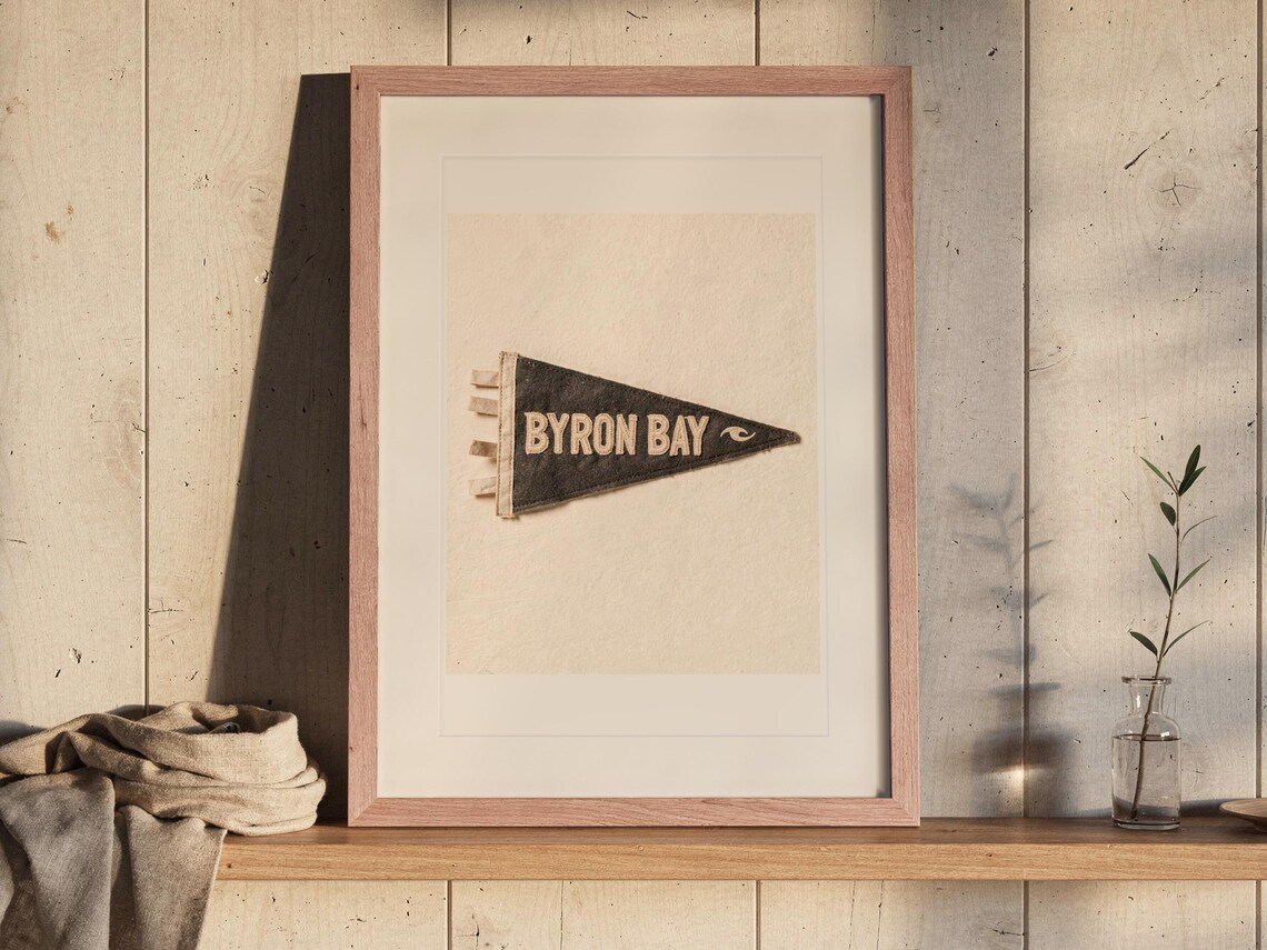 Byron Bay Surf Pennant print in a Red Oak frame with a white mat, leaning on the ledge against the wall in a hallway.
