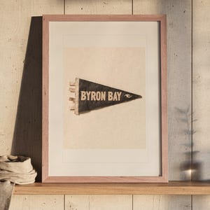 Byron Bay Surf Pennant print in a Red Oak frame with a white mat, leaning on the ledge against the wall in a hallway.