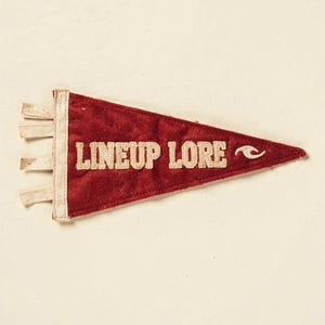 Full Lineup Lore surf pennant artwork on a cream ground, showing the weathered felt texture and stitched lettering