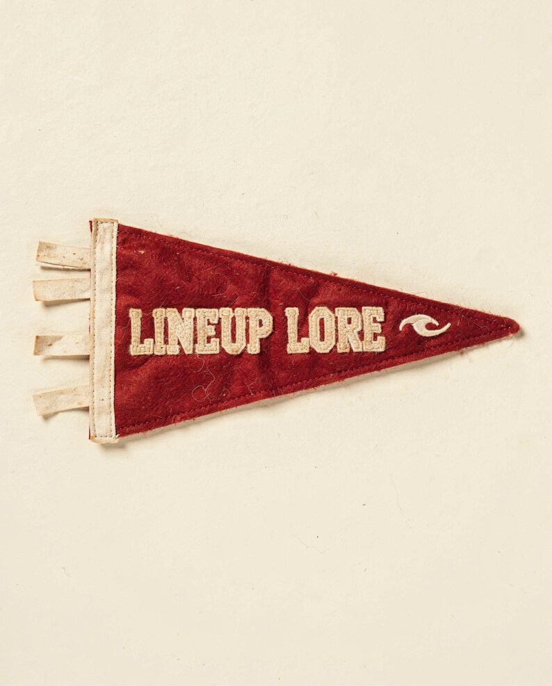 Full Lineup Lore surf pennant artwork on a cream ground, showing the weathered felt texture and stitched lettering