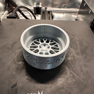 May include: A gray 3D printed model of a car wheel rim with the text "Z-Works Wheels" printed on the side.