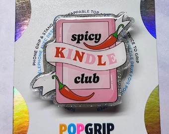 May include: A PopGrip with a pink background featuring the words "spicy KINDLE club" with two red chili peppers. The PopGrip is a phone grip and stand with a wappable top.