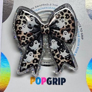 May include: A PopGrip featuring a bow design with a leopard print pattern and white ghost illustrations. The bow is outlined with silver glitter. The PopGrip has a swappable top.