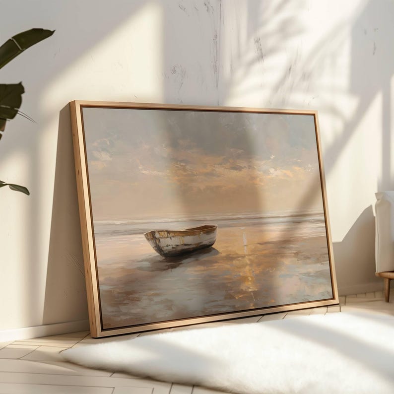 May include: A framed canvas print of a serene beach scene. The artwork depicts a small, weathered boat resting on the shore, with a soft, muted color palette of beige, gray, and gold. The wooden frame adds a natural touch to the artwork.