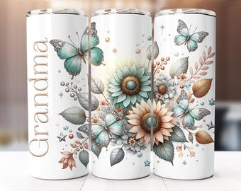 Puede incluir: Un vaso de acero inoxidable blanco con un diseño floral que presenta mariposas, girasoles y hojas en tonos de azul verdoso, marrón y dorado. La palabra "Grandma" está impresa verticalmente en el lado izquierdo del vaso.