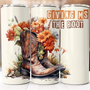 Puede incluir: Un vaso de color crema presenta un diseño de acuarela de botas de vaquero marrones rodeadas de flores naranjas y amarillas. El texto "GIVING MS THE BOOT" se muestra en letras de bloque naranjas y marrones. El vaso está diseñado para contener bebidas.