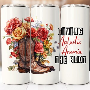 Può includere: Un bicchiere bianco con un design floreale con rose rosse, gialle e arancioni e un paio di stivali da cowboy marroni. Il testo "Giving Aplastic Anemia The Boot" è stampato in lettere nere e rosse.