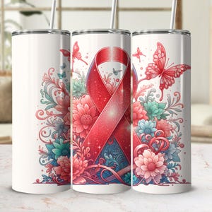 Può includere: Un bicchiere in acciaio inossidabile bianco con un nastro rosso e un design floreale. Il nastro è legato in un fiocco e ha una texture scintillante. I fiori sono rosa, blu e verdi. Ci sono farfalle sul bicchiere.