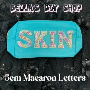 May include: A turquoise blue makeup bag with the word "SKIN" spelled out in large, colorful letters made of macarons. The letters are 5 cm tall.