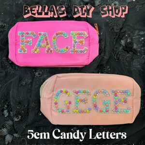 May include: Two pink and peach cosmetic bags with the names "FACE" and "GEGE" spelled out in colorful candy-like letters. The bags are decorated with small, colorful beads. The text "5cm Candy Letters" is written below the bags.