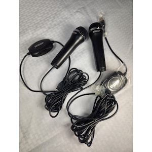 May include: Two black microphones with silver mesh heads and attached black cords. The microphones are connected to a black control box and a USB cable. The brand name "Konami" is visible on the microphones and control box.