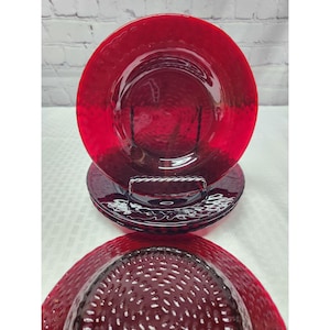 May include: A set of three circular red glass plates featuring a textured, hammered surface pattern. The plates are translucent, allowing light to pass through the vibrant red material, and they are stacked vertically to display the repeating design.
