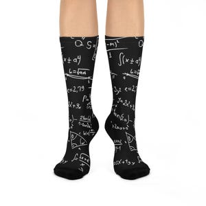 May include: Black socks featuring white mathematical equations and formulas. The equations include symbols, numbers, and geometric shapes. The socks are knee-high and cover the lower legs.