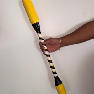 May include: A yellow and black striped club with a black and white striped handle. The club is held by a person. The club is approximately 20 inches long.