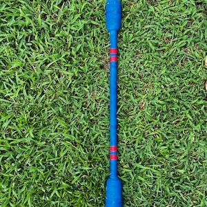 Peut inclure: Un bâton en bois bleu avec des rayures rouges, utilisé pour jouer à un jeu. Le bâton est posé sur une surface herbeuse verte.
