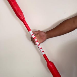 May include: A red baseball bat with a white and red patterned grip. The bat is held by a person. The bat is approximately 30 inches long.