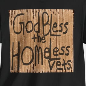 May include: Black t-shirt with a cardboard-style graphic. The graphic features the handwritten text "God Bless the Homeless Vets" in black. The shirt is made of a soft material and has short sleeves.