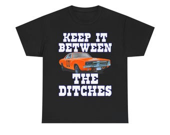 May include: Black t-shirt featuring an orange muscle car with the number 01 and the text "KEEP IT BETWEEN THE DITCHES" in white block letters. The car is a classic model, likely a Dodge Charger.