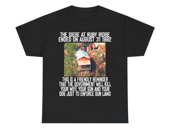 May include: Black t-shirt featuring an image of a building and text. The text reads "THE SIEGE AT RUBY RIDGE ENDED ON AUGUST 31 1992" and "THIS IS A FRIENDLY REMINDER THAT THE GOVERNMENT WILL KILL YOUR WIFE YOUR SON AND YOUR DOG JUST TO ENFORCE GUN LAWS."
