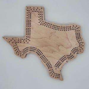 May include: A wooden game board shaped like the state of Texas. The board has a natural wood finish and is decorated with a grid of holes around the perimeter.