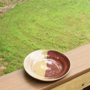 Peut inclure: Un plat en céramique brun et beige de forme arrondie. Le plat est moitié brun et moitié beige, avec une finition lisse et émaillée.