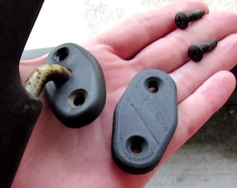 May include: Two black plastic pieces with holes for screws. The pieces are oval shaped and have a textured surface. Two black screws are also shown in the image.
