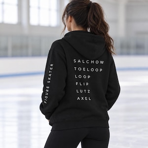 Puede incluir: Una sudadera negra con capucha que presenta texto blanco en la espalda con una lista de saltos de patinaje artístico: SALCHOW, TOELOOP, LOOP, FLIP, LUTZ y AXEL. La manga izquierda tiene el texto blanco FIGURE SKATER impreso verticalmente.