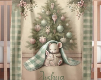 May include: A baby blanket with a Christmas tree design and pastel-coloured ornaments. The blanket has a green and white checked border and features a mouse and bunny under a blanket. The name "Joshua" is written on the blanket.