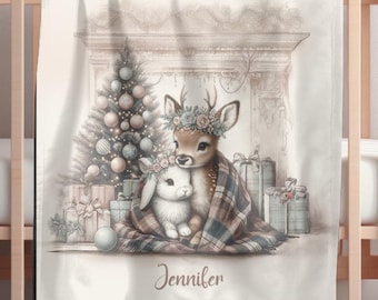 May include: A cream-coloured baby blanket with a watercolour illustration of a deer and a bunny wrapped in a plaid blanket in front of a Christmas tree and gifts. The name "Jennifer" is written below the illustration.