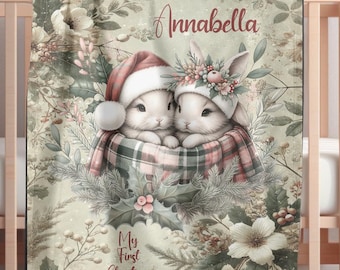 May include: A baby blanket with a watercolour illustration of two bunnies in Christmas attire. The blanket has a floral background and features the name "Annabella" and the text "My First Christmas 2025".