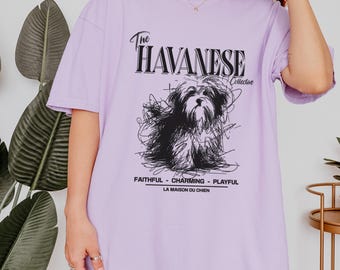 May include: A light purple t-shirt with the text "The Havanese Collective" and a black sketch of a Havanese dog. Below the dog are the words "Faithful - Charming - Playful" and "La Maison Du Chien".