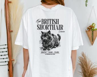 May include: White t-shirt featuring a black and white illustration of a British Shorthair cat. The text "The British Shorthair" and "Collective" are above the cat image. Below the cat, the text reads "GENTLE - CALM - PLUSH" and "LA MAISON DU CHAT."