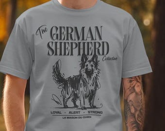 May include: A gray t-shirt featuring a sketch of a German Shepherd dog. The text "The German Shepherd Collective" is above the dog, with "Loyal - Alert - Strong" and "La Maison Du Chien" below.