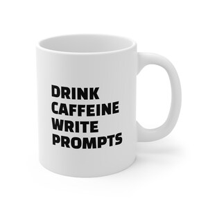 May include: White ceramic coffee mug with black text that reads "DRINK CAFFEINE WRITE PROMPTS".