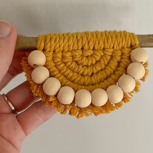 May include: A small, yellow macrame wall hanging with a wooden dowel at the top and a fringe of wooden beads around the bottom.