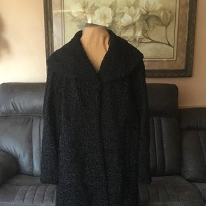 May include: A long black fur coat with a large collar. The coat is on a mannequin and is in front of a sofa.